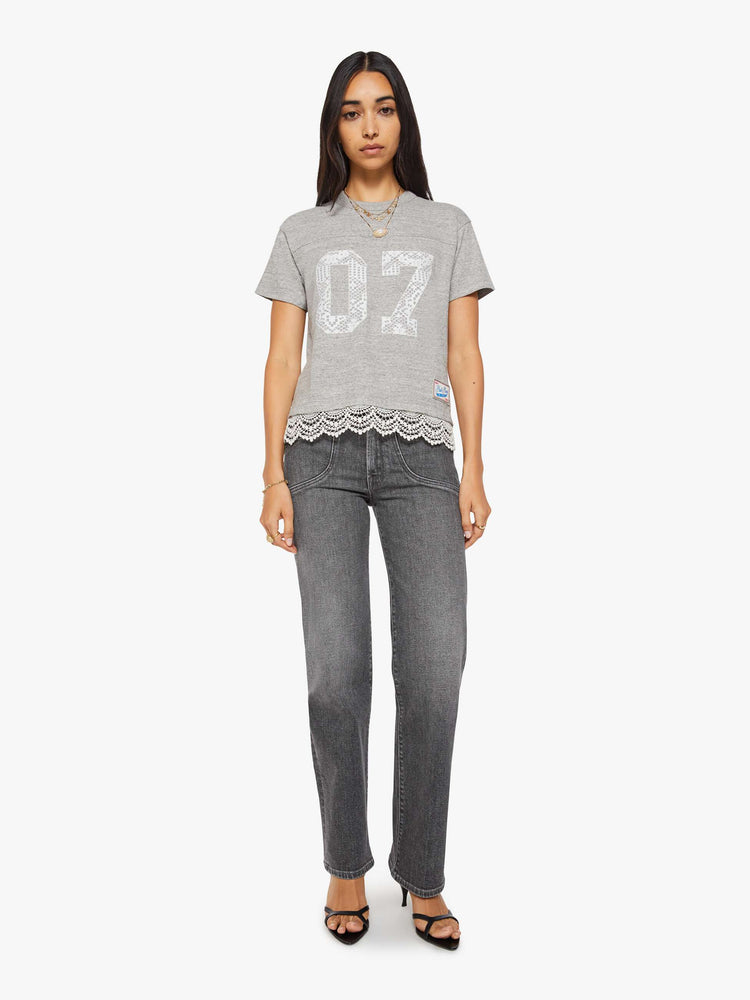 Full body view of a woman in a heather grey with white lace applique on the front and lace trim oversized crewneck tee is designed with drop shoulders, short sleeves and a boxy fit.