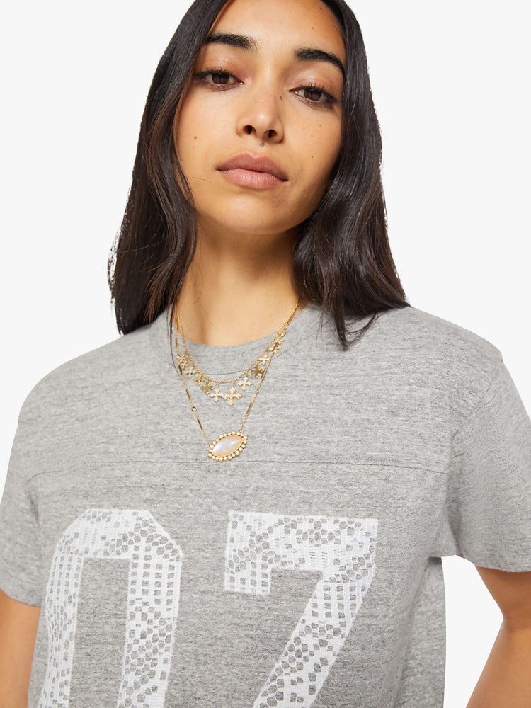 Close up view of a woman in a heather grey with white lace applique on the front and lace trim oversized crewneck tee is designed with drop shoulders, short sleeves and a boxy fit.