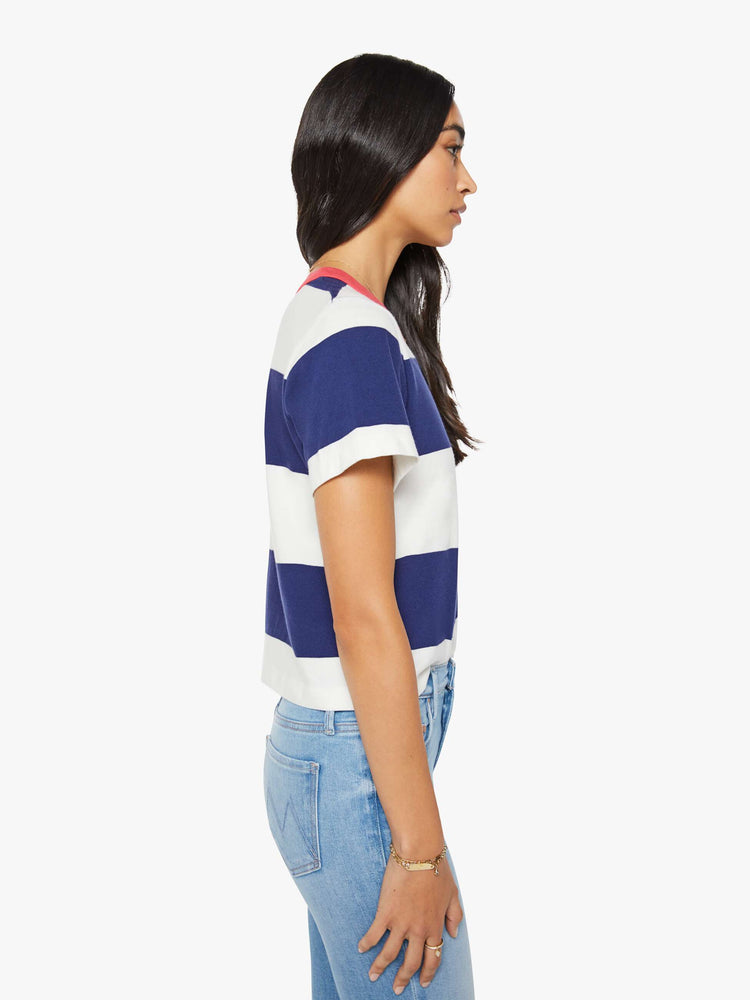 Side view of the woman in a white and navy stripes with a faded red trim collar tee with a chest  inspired by a country club logo.
