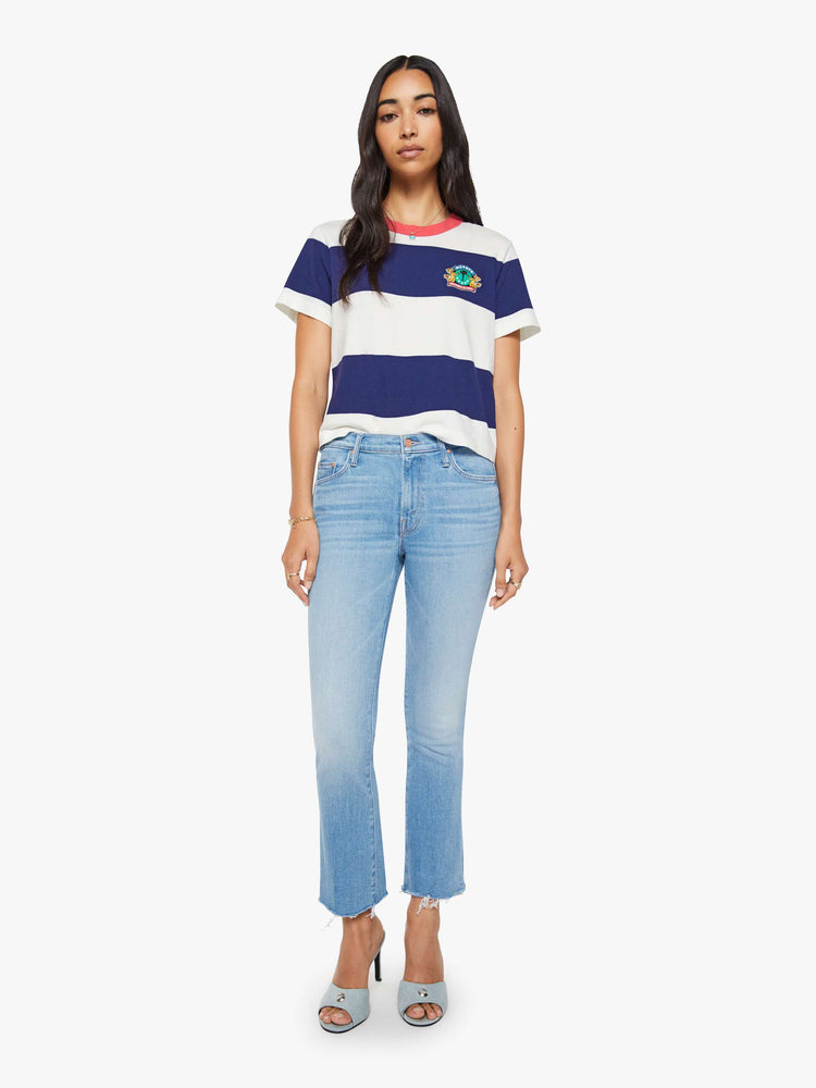 Full body view of the woman in a white and navy stripes with a faded red trim collar tee with a chest  inspired by a country club logo.