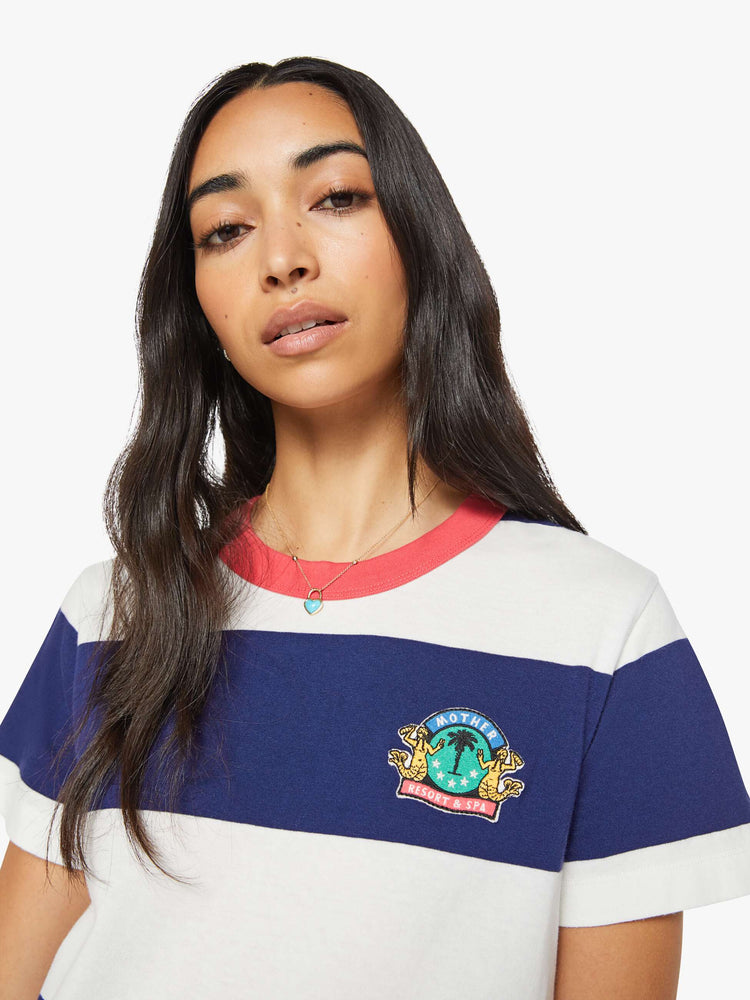 Close up view of the woman in a white and navy stripes with a faded red trim collar tee with a chest  inspired by a country club logo.