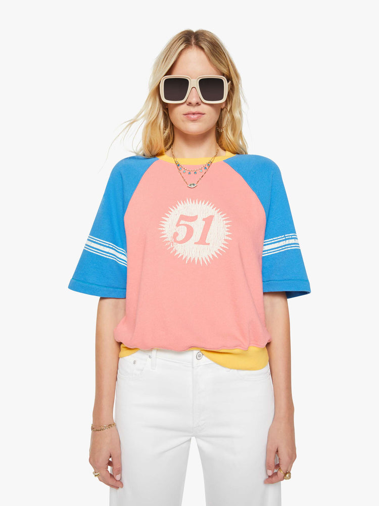 Front view of a woman in a pale pink with blue sleeves and yellow trim sweatshirt and features a crackle-printed 51 on the chest and white stripes on the sleeves.