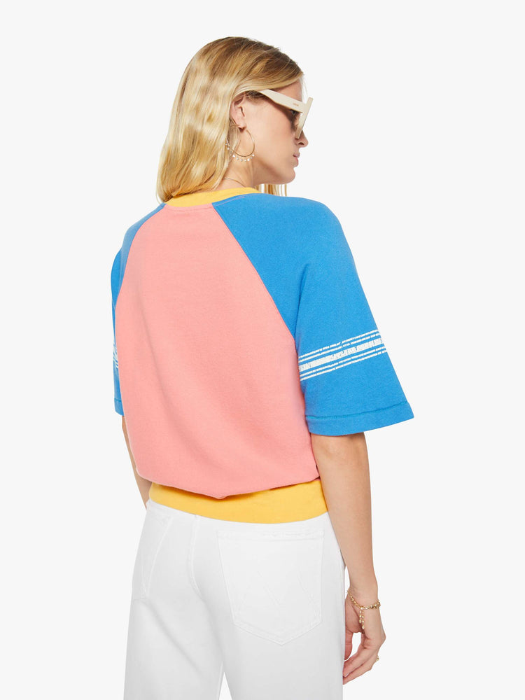 Back view of a woman in a pale pink with blue sleeves and yellow trim sweatshirt and features a crackle-printed 51 on the chest and white stripes on the sleeves.
