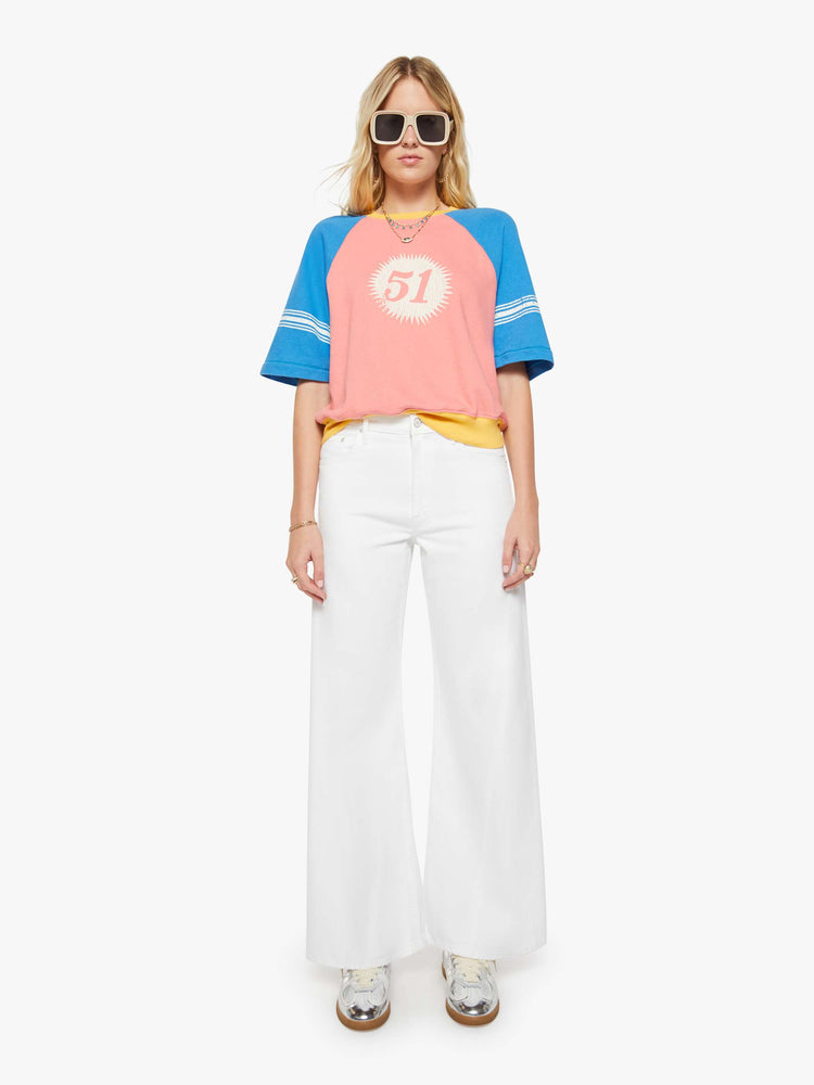 Full body view of a woman in a pale pink with blue sleeves and yellow trim sweatshirt and features a crackle-printed 51 on the chest and white stripes on the sleeves.
