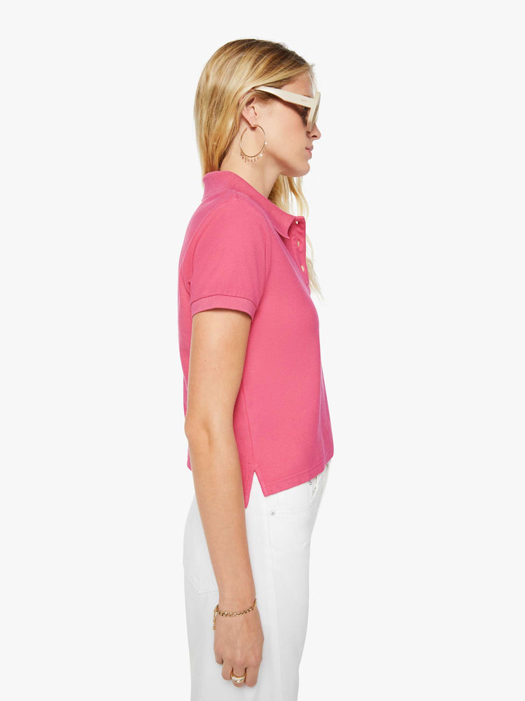 Side view of a woman in pink polo shirt with a three-button placket, short sleeves, split hem and a slightly shrunken fit.