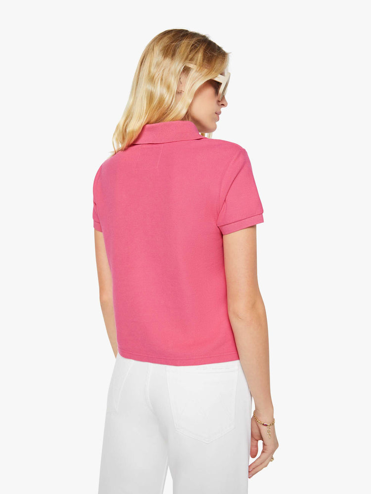 Back view of a woman in pink polo shirt with a three-button placket, short sleeves, split hem and a slightly shrunken fit.