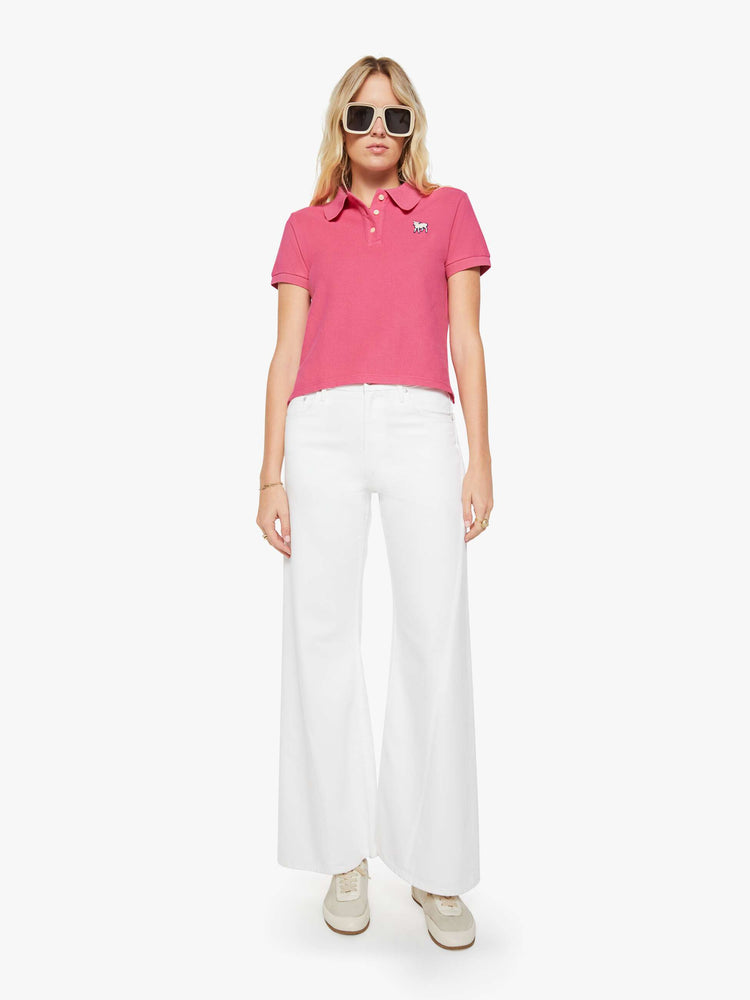 Full body view of a woman in pink polo shirt with a three-button placket, short sleeves, split hem and a slightly shrunken fit.