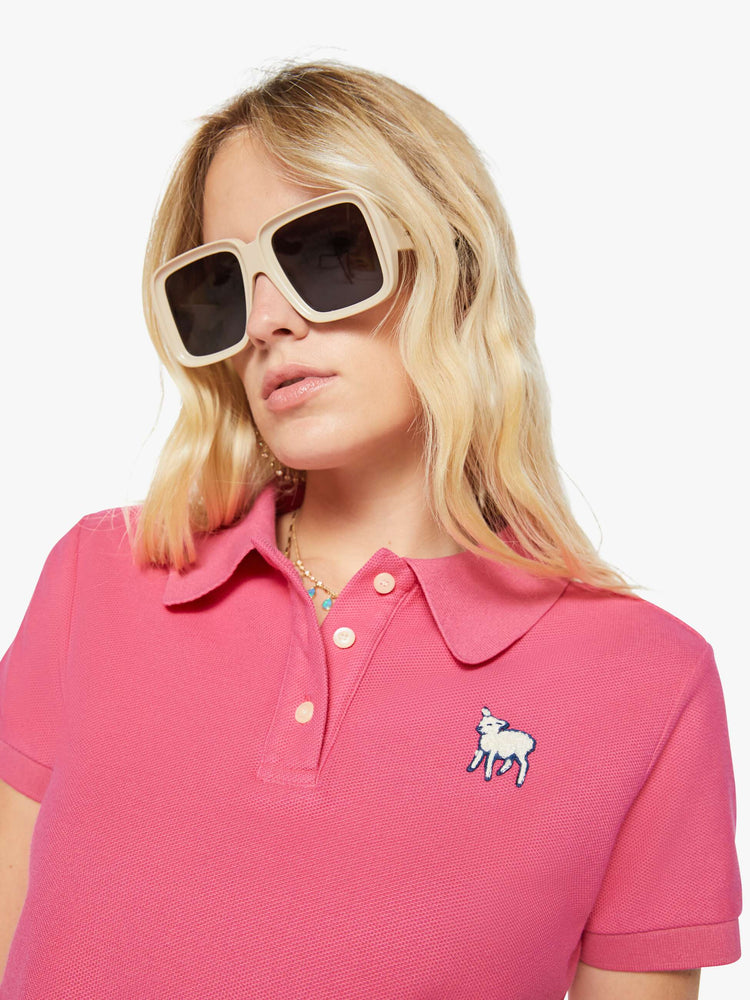 Close up view of a woman in pink polo shirt with a three-button placket, short sleeves, split hem and a slightly shrunken fit.