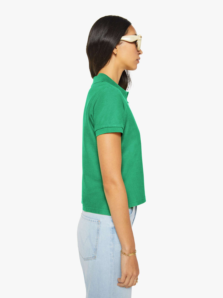 Side view of a woman in green polo shirt with a three-button placket, short sleeves, split hem and a slightly shrunken fit.