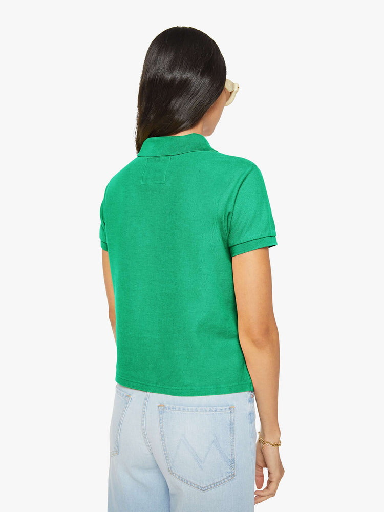 Back view of a woman in green polo shirt with a three-button placket, short sleeves, split hem and a slightly shrunken fit.