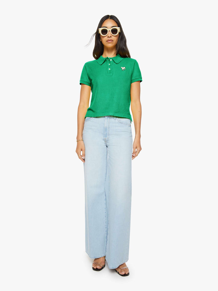 Full body view of a woman in green polo shirt with a three-button placket, short sleeves, split hem and a slightly shrunken fit.
