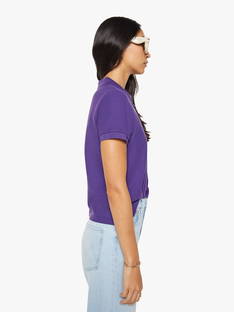 Side view of a woman in purple polo shirt with a three-button placket, short sleeves, split hem and a slightly shrunken fit.