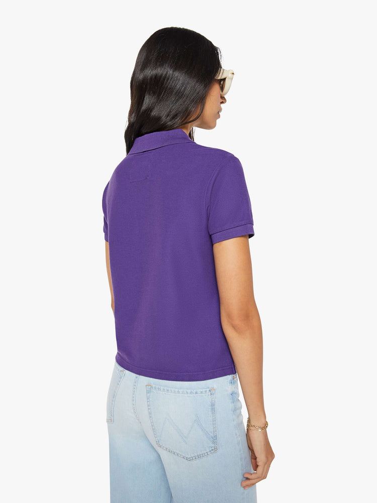Back view of a woman in purple polo shirt with a three-button placket, short sleeves, split hem and a slightly shrunken fit.