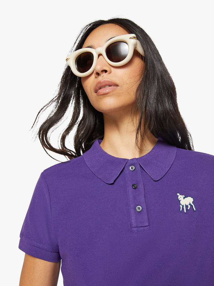 Close up view of a woman in purple polo shirt with a three-button placket, short sleeves, split hem and a slightly shrunken fit.
