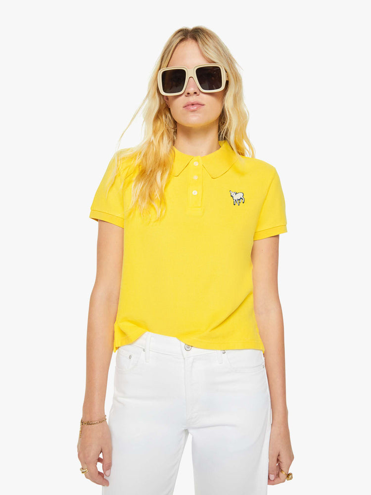 Front view of a woman in yellow polo shirt with a three-button placket, short sleeves, split hem and a slightly shrunken fit.