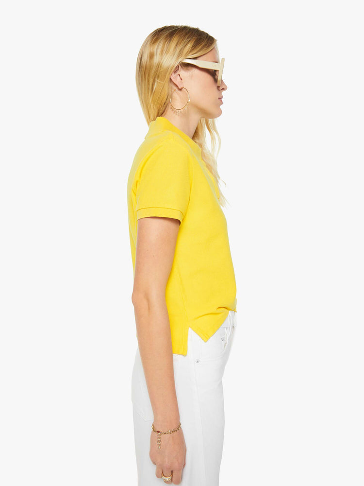 Side view of a woman in yellow polo shirt with a three-button placket, short sleeves, split hem and a slightly shrunken fit.