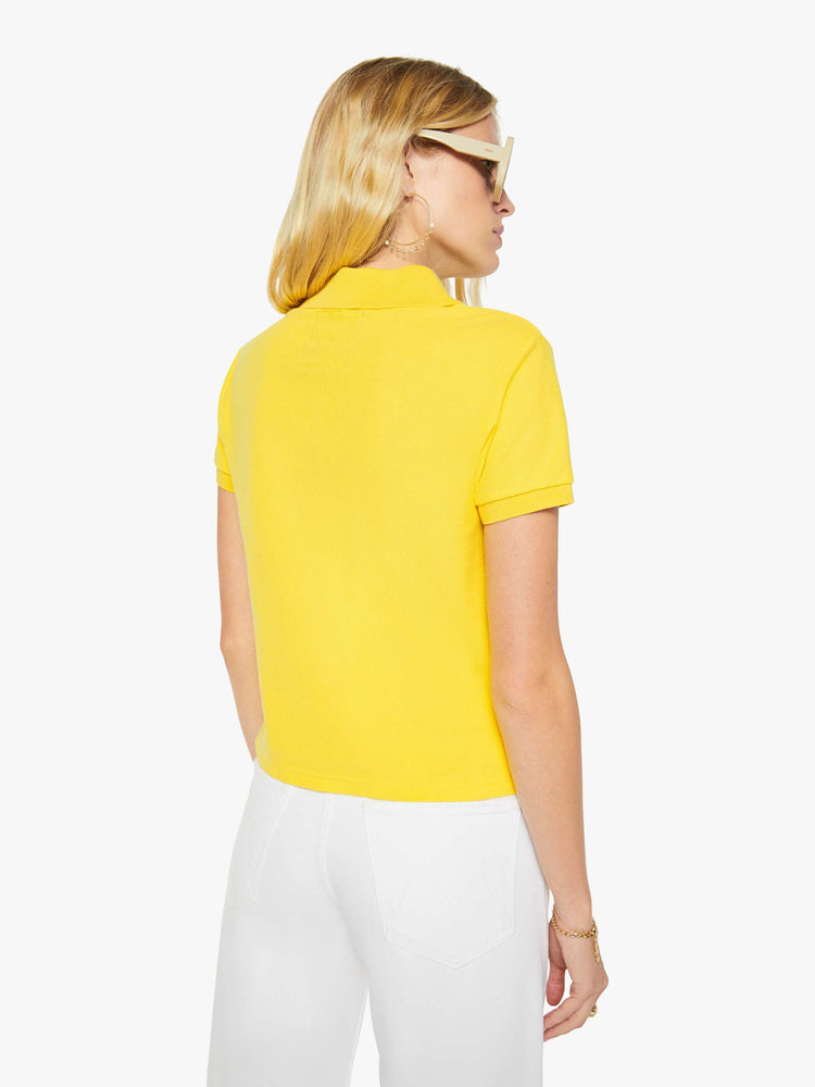 Back view of a woman in yellow polo shirt with a three-button placket, short sleeves, split hem and a slightly shrunken fit.
