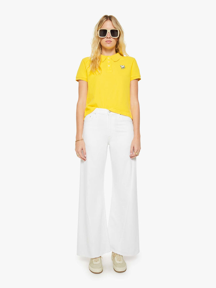 Full body view of a woman in yellow polo shirt with a three-button placket, short sleeves, split hem and a slightly shrunken fit.