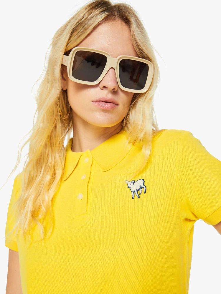 Close up view of a woman in yellow polo shirt with a three-button placket, short sleeves, split hem and a slightly shrunken fit.