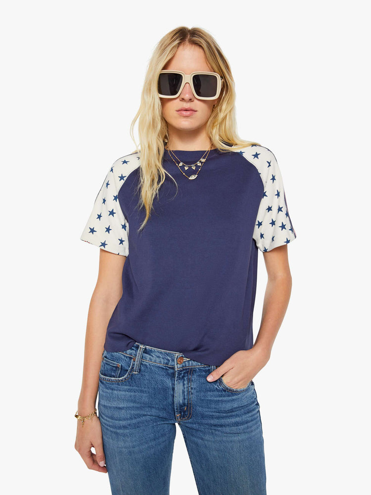 Front view of a woman in navy blue with white sleeves decorated with stars and stripes in crewneck raglan tee with short sleeves and a boxy fit.