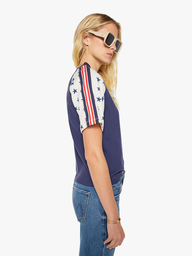 Side view of a woman in navy blue with white sleeves decorated with stars and stripes in crewneck raglan tee with short sleeves and a boxy fit.