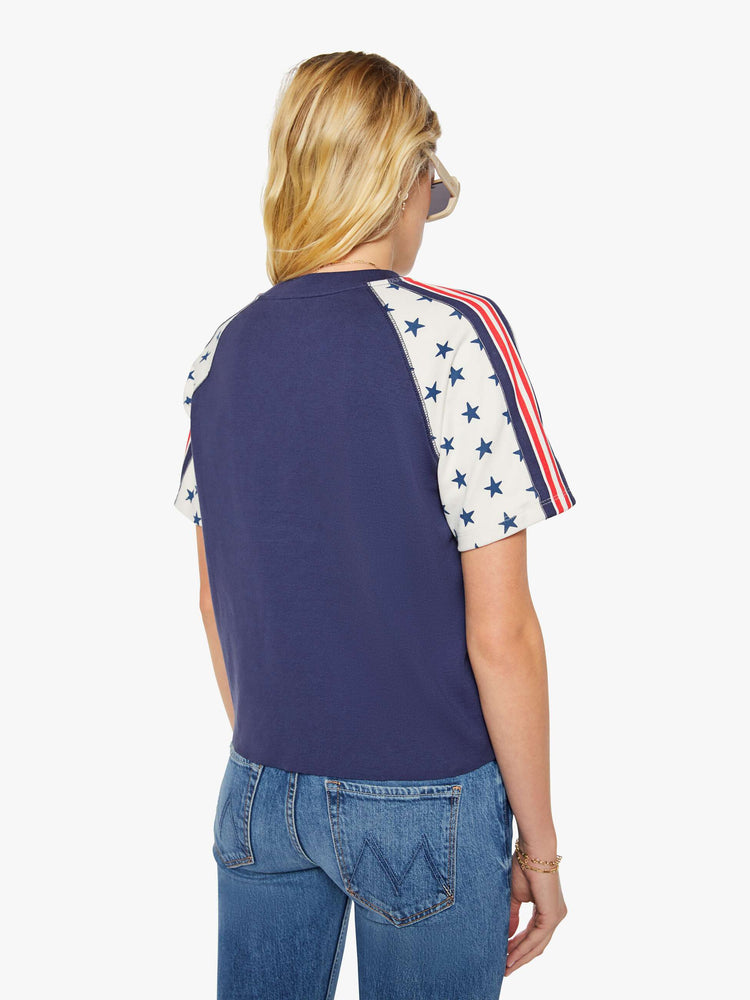 Back view of a woman in navy blue with white sleeves decorated with stars and stripes in crewneck raglan tee with short sleeves and a boxy fit.