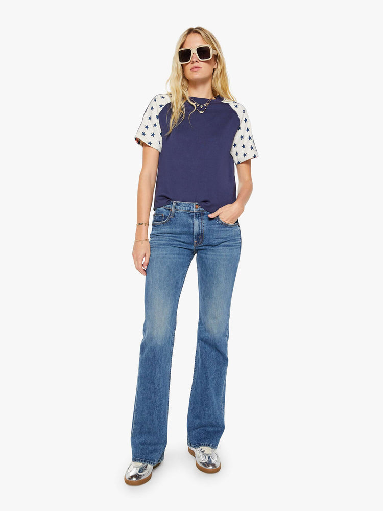Full body view of a woman in navy blue with white sleeves decorated with stars and stripes in crewneck raglan tee with short sleeves and a boxy fit.