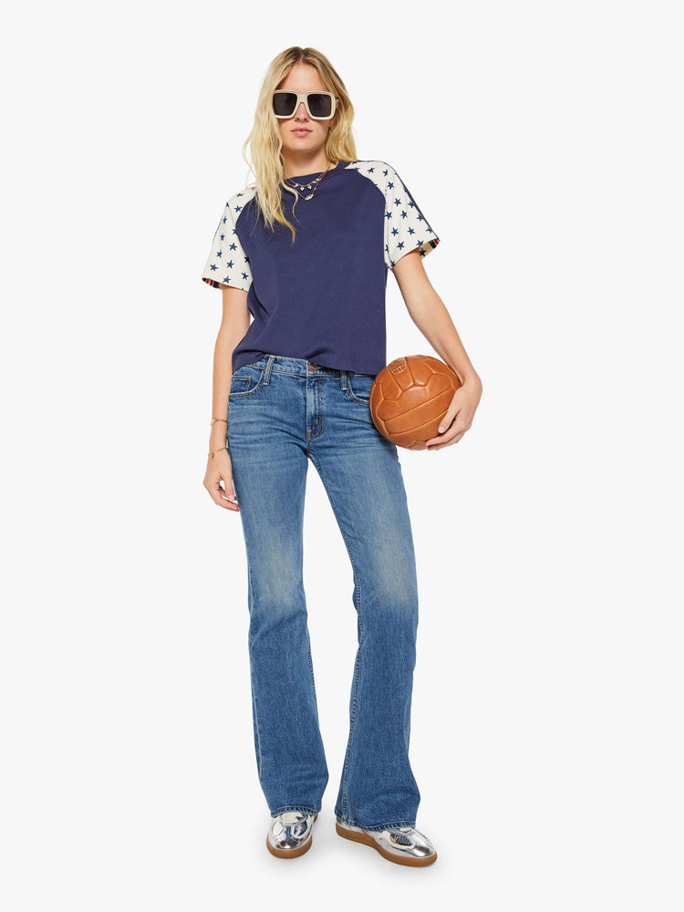 Full body view of a woman in navy blue with white sleeves decorated with stars and stripes in crewneck raglan tee with short sleeves and a boxy fit.