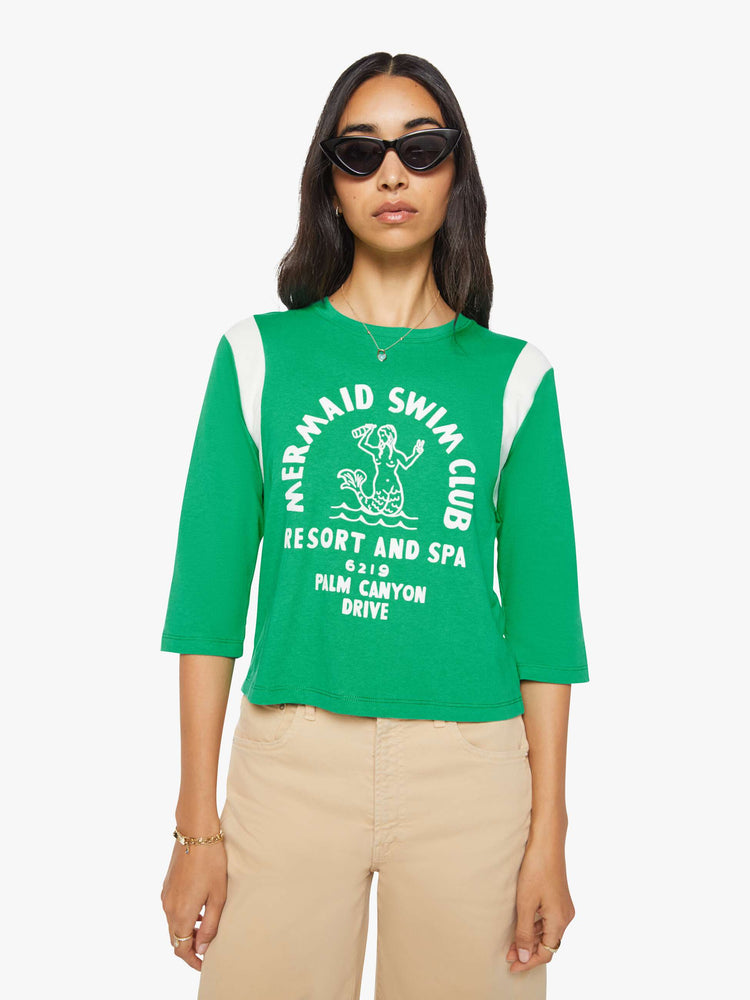 Front view of a woman in green with white inserts at the sleeves tee with a flocked swim club graphic on the front and text in white on the back.