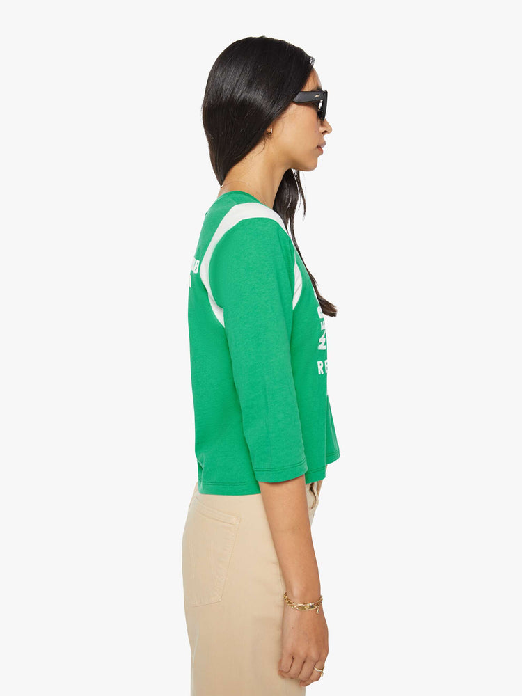 Side view of a woman in green with white inserts at the sleeves tee with a flocked swim club graphic on the front and text in white on the back.