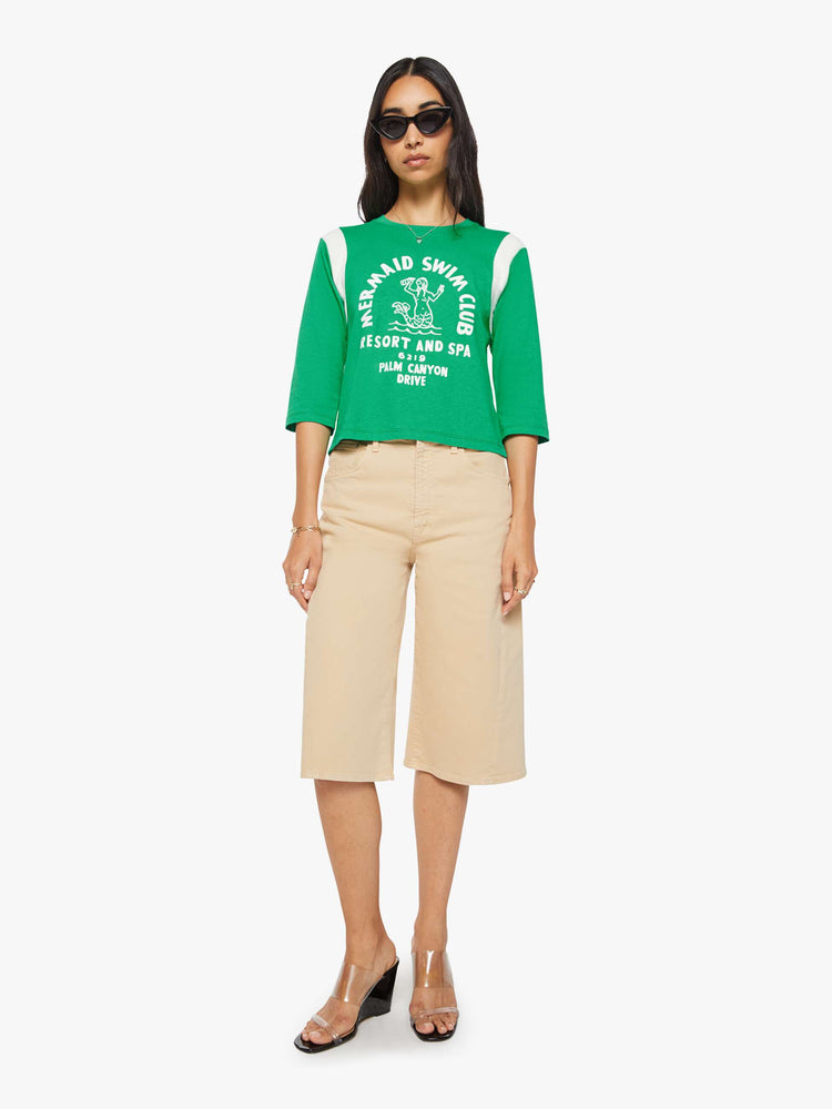 Full body view of a woman in green with white inserts at the sleeves tee with a flocked swim club graphic on the front and text in white on the back.