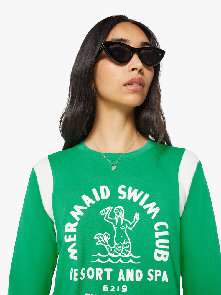 Close up view of a woman in green with white inserts at the sleeves tee with a flocked swim club graphic on the front and text in white on the back.