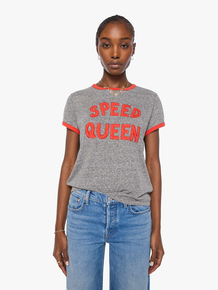 Front view of a woman in a heathered grey tee features red trim and an applique text graphic with small metal studs on the front.