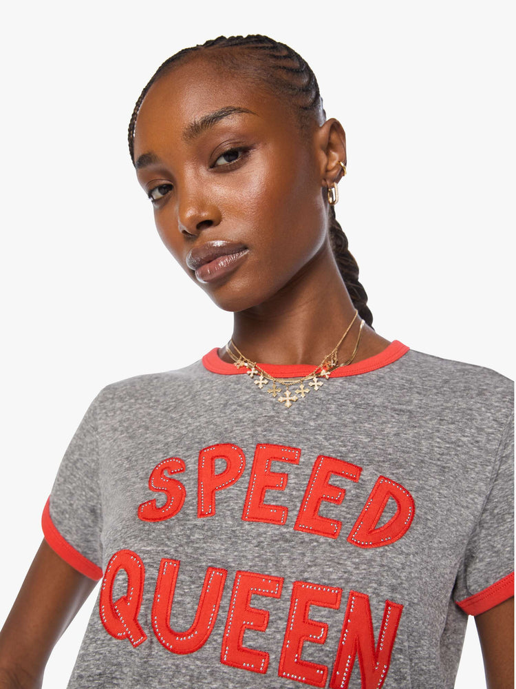 Close up view of a woman in a heathered grey tee features red trim and an applique text graphic with small metal studs on the front.