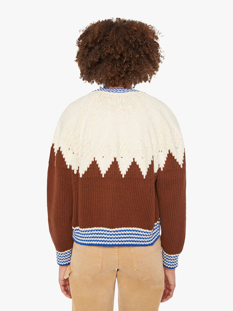 Back view of a woman in a half cream, half brown with a zig-zag pattern and blue-and-white-striped hems cardigan.