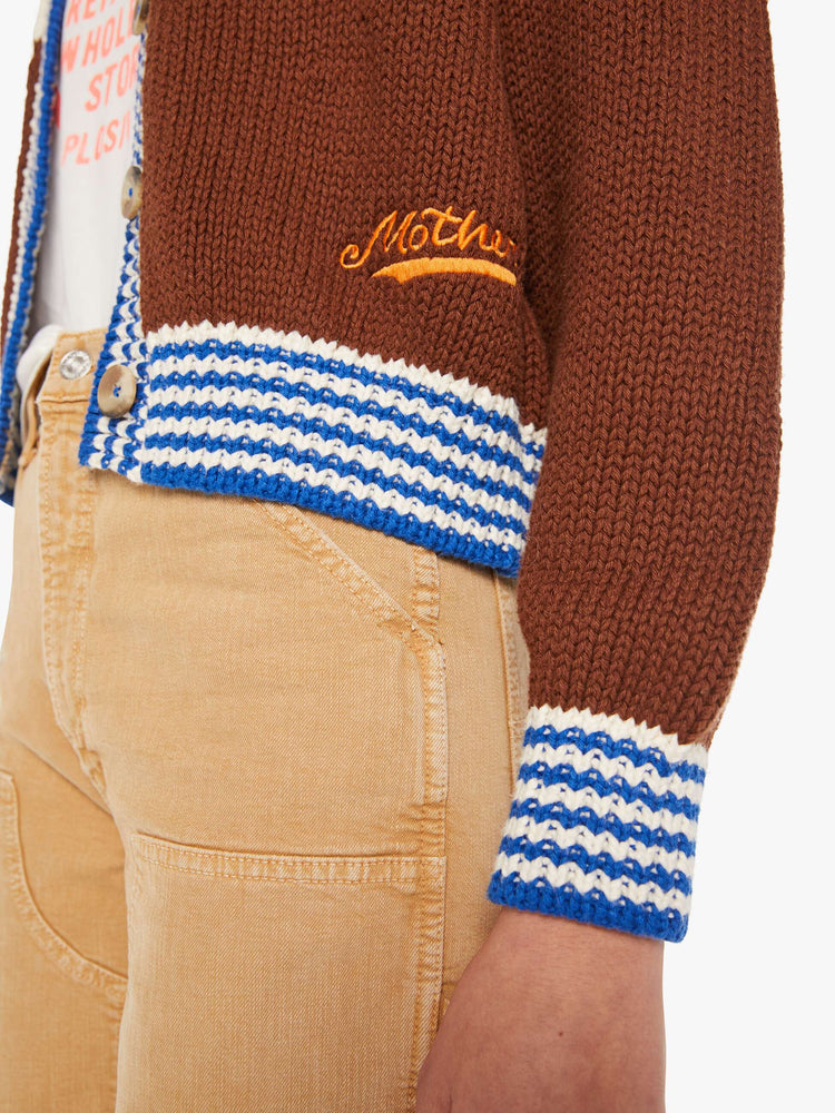 Swatch view of a woman in a half cream, half brown with a zig-zag pattern and blue-and-white-striped hems cardigan.