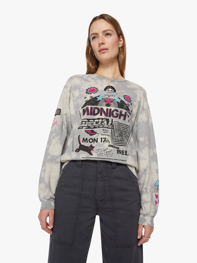 Front view of a woman light grey with bleached sweatshirt with dropped sleeves with a blue, black and pink graphics on the chest and sleeves inspired by a concert flyer.