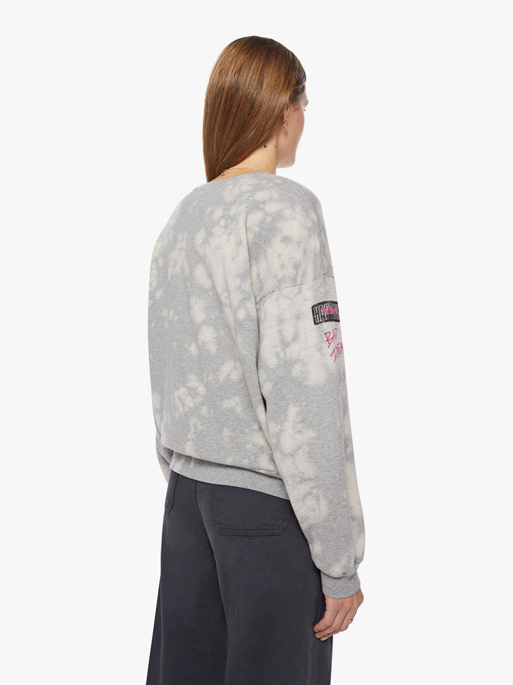 Back view of a woman light grey with bleached sweatshirt with dropped sleeves with a blue, black and pink graphics on the chest and sleeves inspired by a concert flyer.