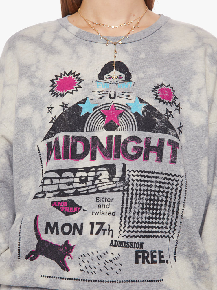 Close up view of a woman light grey with bleached sweatshirt with dropped sleeves with a blue, black and pink graphics on the chest and sleeves inspired by a concert flyer.