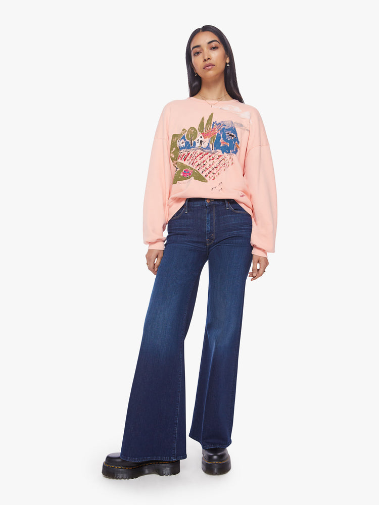 Full body view of a woman light pink sweatshirt with dropped sleeves with a hand-drawn doodle of a barn in flames.