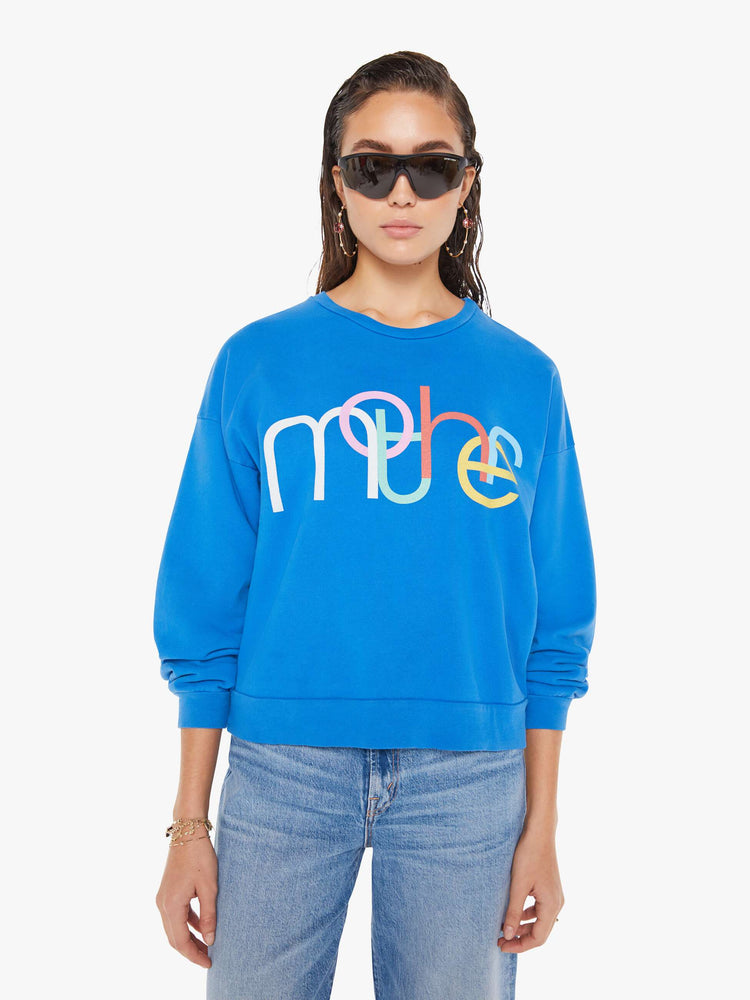 Front view of a woman wearing a bright blue oversized sweatshirt featuring a colorful graphic reading "mother", paired with a medium blue wash jean.