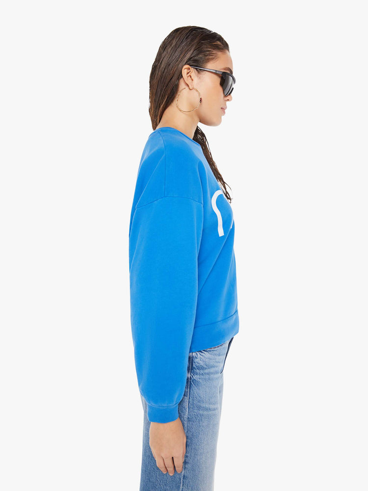 Side view of a woman wearing a bright blue oversized sweatshirt, paired with a medium blue wash jean.