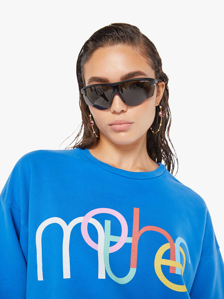 Front close up view of a woman wearing a bright blue oversized sweatshirt featuring a colorful graphic reading "mother".