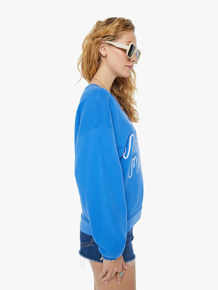 A side view of a woman wearing a blue sweatshirt featuring an oversized fit, paired with dark blue denim short.