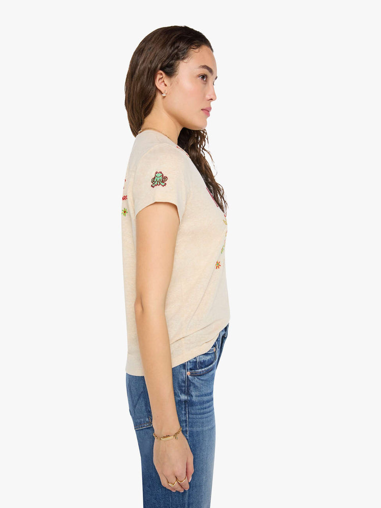 Side view of a woman in cream with maroon applique text and colorful embroidery at the chest.