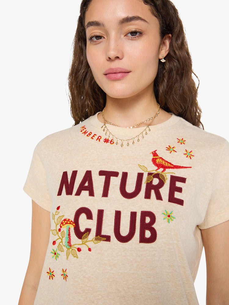 Close up view of a woman in cream with maroon applique text and colorful embroidery at the chest.