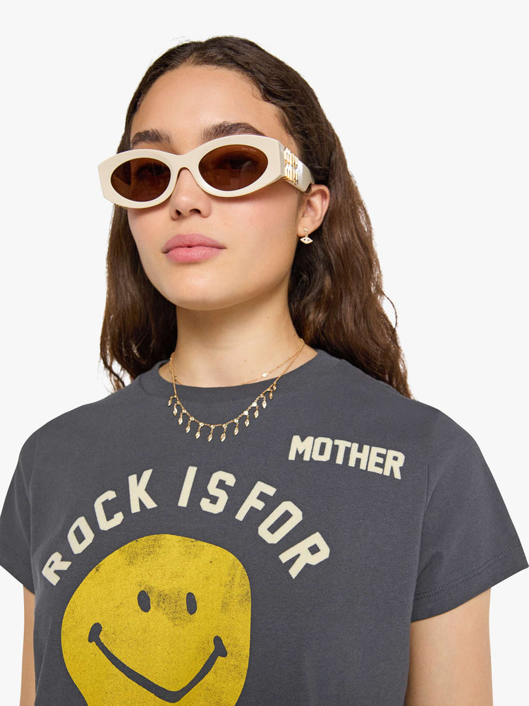 Close up view of a woman in faded black tew with a smiley-face graphic and flocked text in white across the chest.