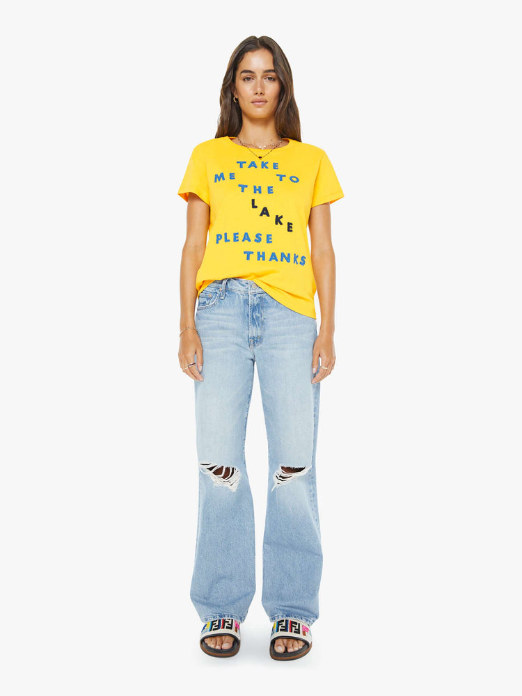 Full body view of a woman in a  yellow tee with a blue text graphic on the front.