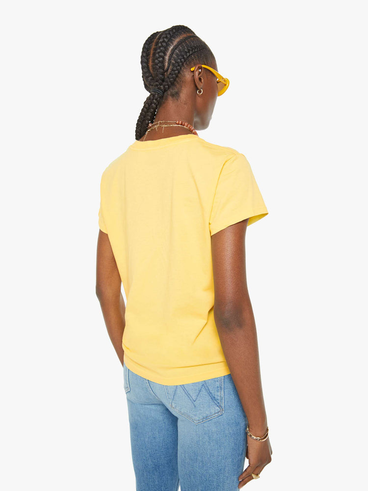 Back view of a woman in a yellow crewneck tee with a tropical storefront graphic in red and blue on the front.