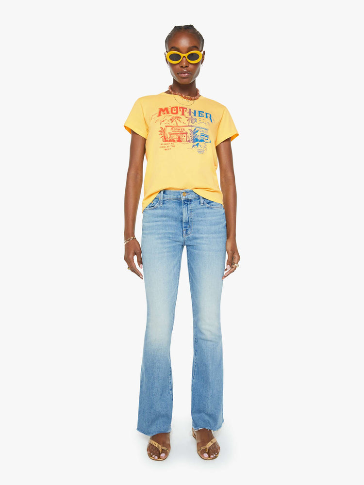 Full body view of a woman in a yellow crewneck tee with a tropical storefront graphic in red and blue on the front.